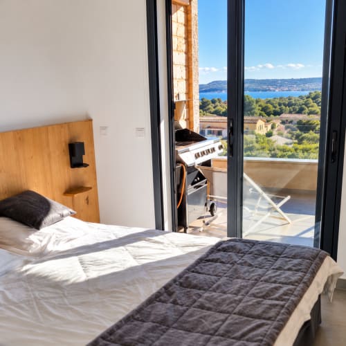Chambre moderne avec terrasse vue mer aux Villas d'A Storia, Corse : lit, tête de lit en bois, ambiance méditerranéenne