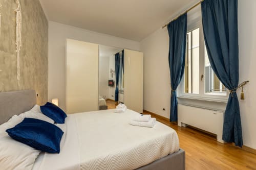 Camera luminosa al Buonanotte Colosseo Roma con letto matrimoniale, cuscini blu velluto, tende blu navy e pavimento in legno
