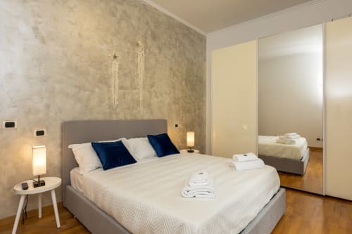 Camera da letto moderna dell'appartamento Buonanotte Colosseo Roma con letto grigio, guardaroba specchiato e vista sulla città