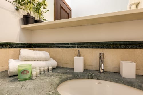 Bancone del bagno dell'appartamento Buonanotte Colosseo a Roma con articoli da toilette, asciugamani, candele e superficie in marmo grigio