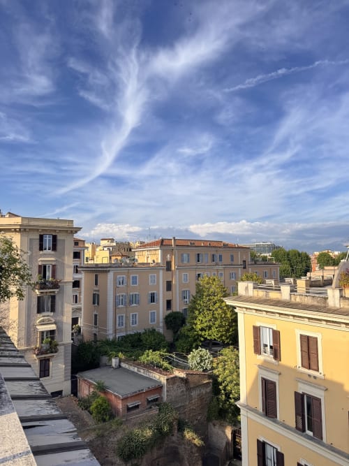 Storici edifici residenziali romani con facciate in terracotta calda e persiane blu sotto un cielo luminoso, vista della città