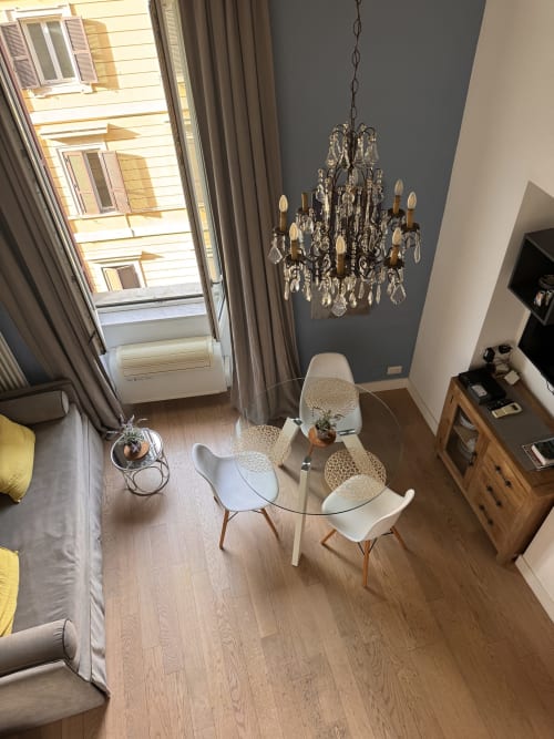 Modern dining area at Buonanotte Colosseo Rome with round table, white chairs, crystal chandelier, and city views through