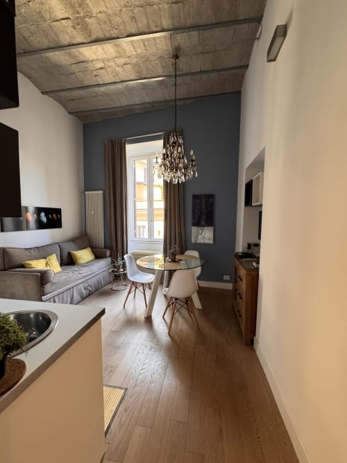 Moderno monolocale a Buonanotte Colosseo a Roma con pareti grigie, travi in legno a vista, lampadario di cristallo e zona pranzo