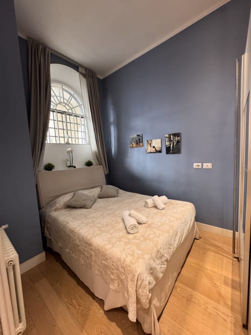 Camera da letto moderna con pareti blu, finestra ad arco e biancheria crema a Buonanotte Colosseo a Roma