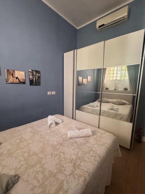 Camera moderna a Buonanotte Colosseo Roma con armadio specchiato, pareti blu e finestra con vista sulla città