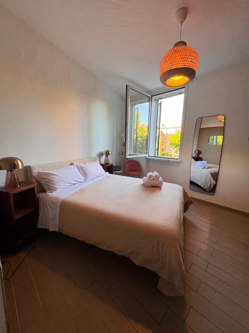 Modern studio apartment bedroom at Buonanotte Colosseo in Rome with queen bed, orange pendant lamp, and city views through