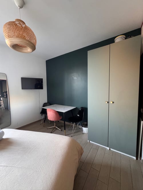 Moderno monolocale a Roma con letto, scrivania, parete accent verde, armadio e lampada a sospensione intrecciata
