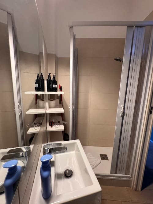 Bagno moderno con lavabo bianco, box doccia e scaffali a parete nell'appartamento Buonanotte Colosseo a Roma