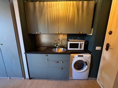 Piccola cucina moderna in appartamento a Roma con mobili in acciaio inox, piano di lavoro nero, microonde e lavatrice