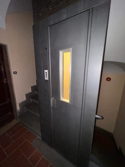 Moderno ascensore grigio con pannello porta giallo illuminato nello studio Garibaldi dell'hotel Buonanotte Colosseo, Roma