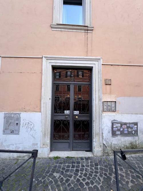 Ingresso di edificio storico a Roma con maestose porte in ferro e facciata color pesca, Buonanotte Colosseo