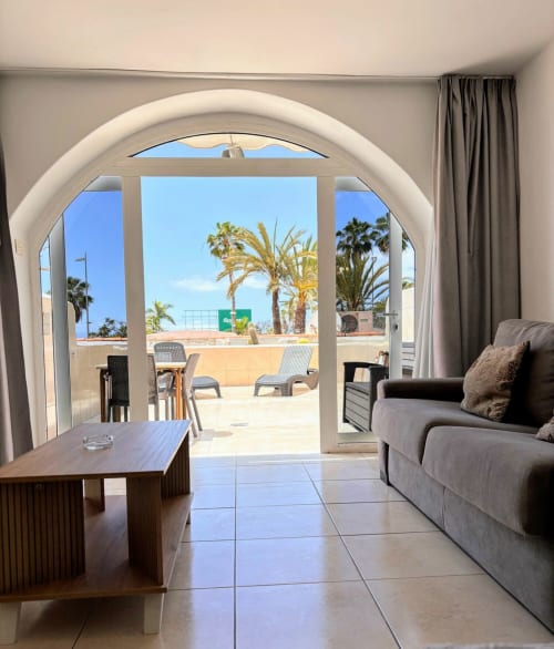 Bright studio apartment at Paraiso Royal with arched doors opening to terrace, palm trees, and sea views in Playa de las