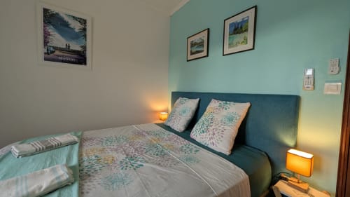 Bedroom at La Maison Des Hôtes with turquoise accent wall, teal headboard, patterned bedding, warm lighting, and framed