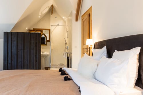Modern bedroom at Domaine du Tertre Ychot with ensuite bathroom, white bedding, dark headboard, and sloped ceiling