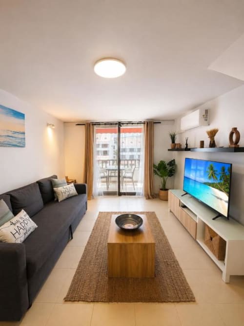 Modern apartment living room in Playa de las Américas with black sofa, TV, wooden coffee table, and balcony view