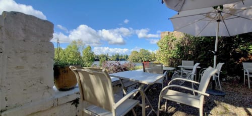 Terrasse extérieure de la Villa Aliénor aux Andelys avec vue sur la rivière, table à manger, parasols et chaises longues