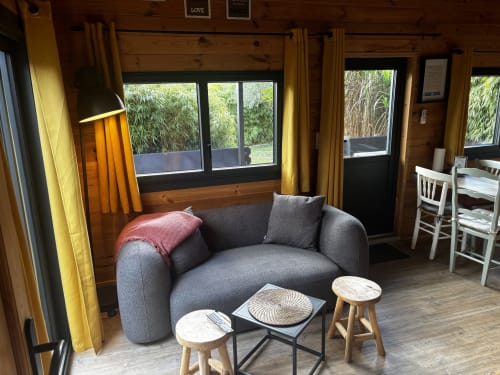 Intérieur cosy de gîte en bois aux Gîtes D'armor avec fauteuil gris, vue sur bambous et charme rustique à Tréguidel, France