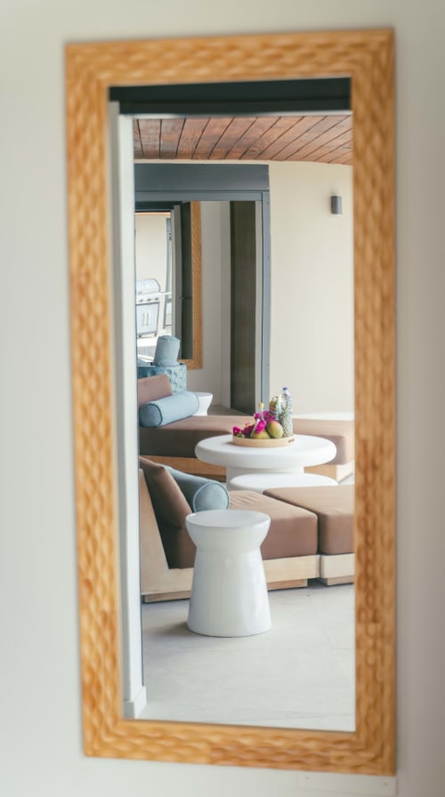 Miroir à cadre bois reflétant l'espace de vie moderne de la villa avec tables d'appoint blanches et fleurs roses à la Collection Blue Horizon