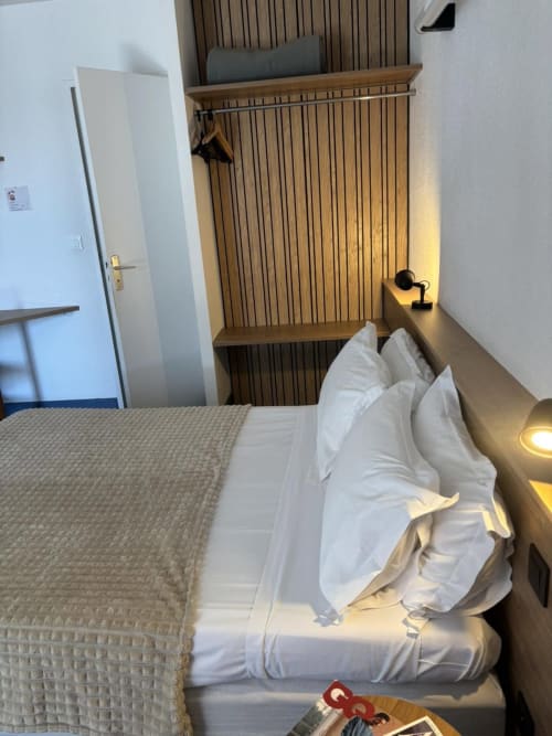 Chambre moderne de l'Hôtel Du Rocher au Caylar avec lit, tête de lit en bois, bureau et porte blanche