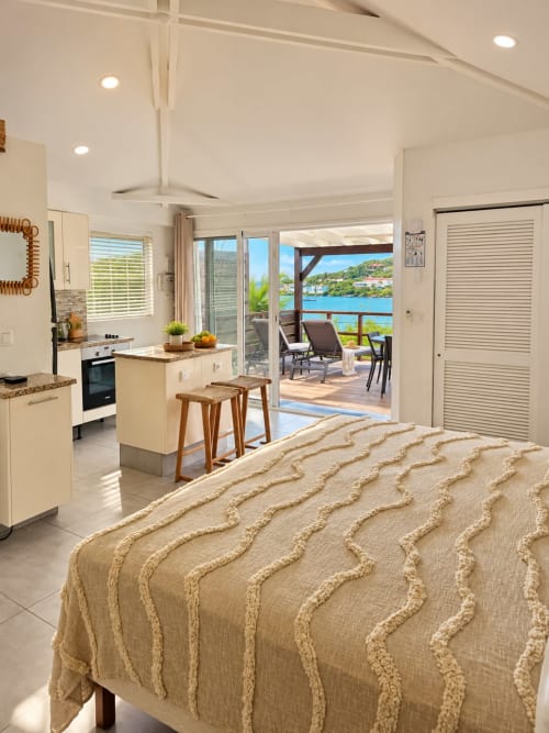 Bright beachfront bungalow studio in Saint-Martin with sea view, open kitchen, bed with beige throw, and terrace access