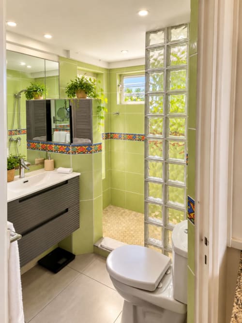 Modern bathroom with lime green tiles, dark vanity, walk-in shower with glass blocks, and potted plants at Les Balcons