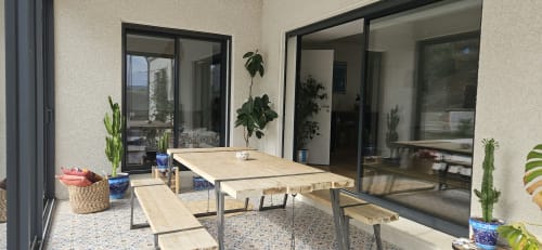 Terrasse moderne de la Villa Azura à Carcassonne avec table en bois, banquettes, plantes en pots et portes vitrées