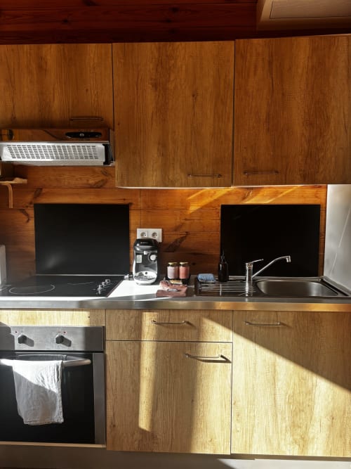 Cuisine en bois du gîte Gîtes d'Armor avec évier inox, plaque de cuisson, four et deux écrans noirs à Tréguídel
