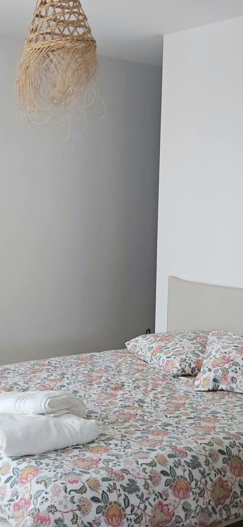 Chambre moderne à la Villa Azura, Carcassonne, avec parure florale, serviettes blanches, luminaire suspendu tressé et décor épuré