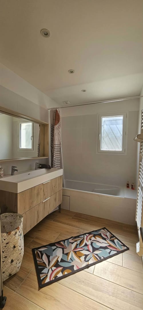 Salle de bain moderne à la Villa Azura, Carcassonne avec vasque en bois, baignoire blanche, miroir et tapis décoratif