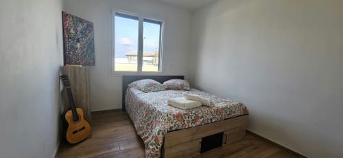 Chambre douillette avec lit double, parure florale, guitare en bois et grande fenêtre avec vue sur Carcassonne à Villa Azura