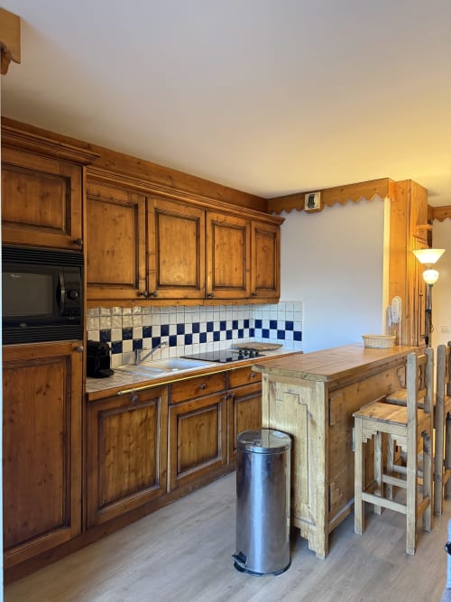 Cuisine en bois avec crédence carrelée bleu et blanc, îlot avec coin repas et micro-ondes dans l'appartement La Plagne Ski Confort