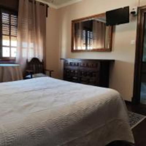 Acogedora habitación doble en Pension Castio de Santillana del Mar con ropa de cama blanca, TV, espejo y vistas a las montañas