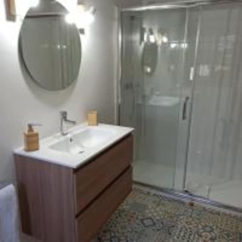 Baño moderno del hotel Pensión Castio en Santillana del Mar con tocador de madera, lavamanos blanco, espejo redondo y ducha de cristal