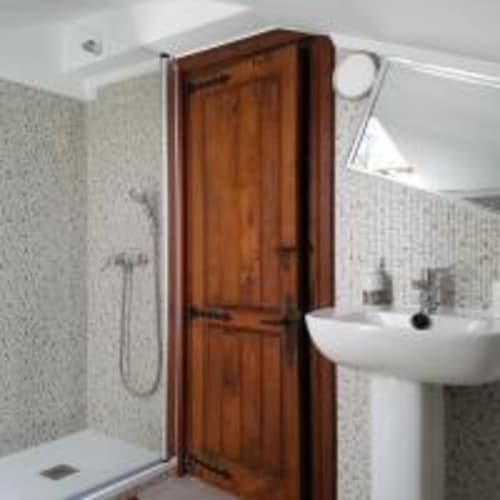 Baño de la Pensión Castio en Santillana del Mar con puerta de madera, lavabo blanco, área de ducha y paredes alicatadas