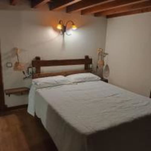 Habitación doble en Pensión Castio en Santillana del Mar con cama de madera, sábanas blancas, vigas vistas y vistas al jardín