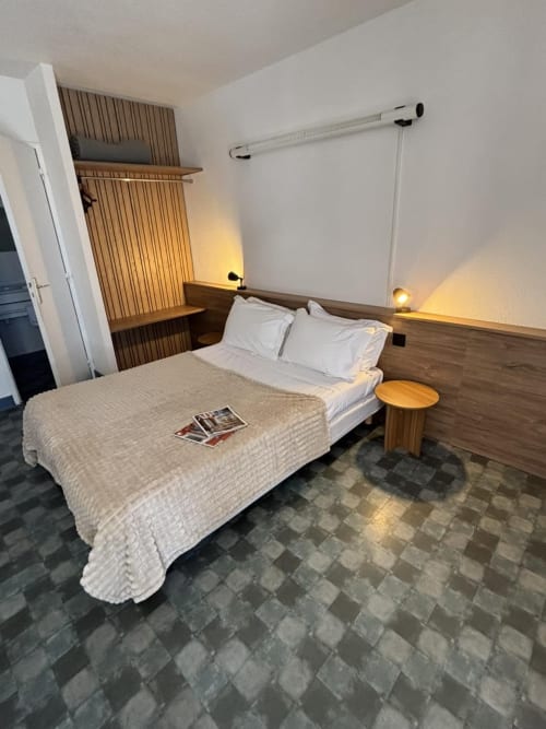 Chambre moderne de l'Hôtel Du Rocher avec lit double, tête de lit en bois, bureau et vue sur la ville du Caylar