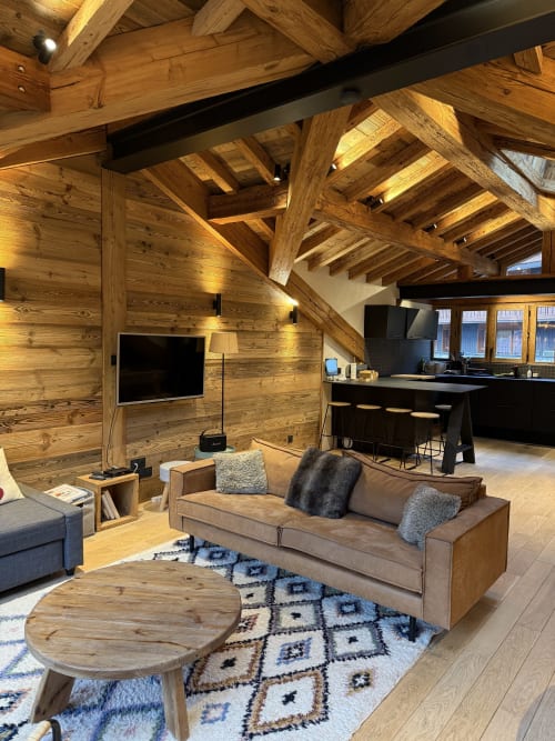 Intérieur de chalet moderne à La Plagne avec poutres apparentes, canapé taupe, téléviseur, cuisine et tapis géométrique dans un appartement de ski