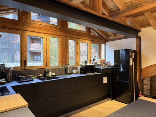 Cuisine moderne aux armoires noires, poutres apparentes et grandes fenêtres panoramiques sur les montagnes à La Plagne-Tarentaise