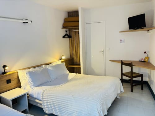 Chambre Triple Bright Confort à l'Hôtel Du Rocher au Caylar : lit blanc, bureau, TV et vue sur la ville