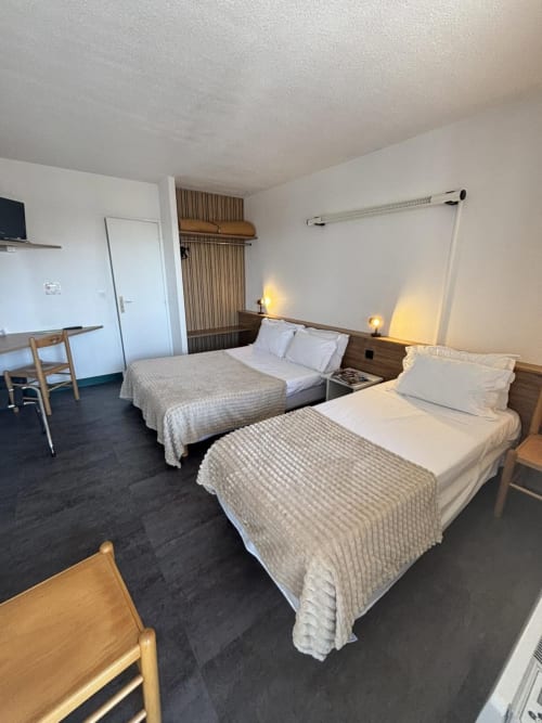 Chambre triple de l'Hôtel Du Rocher au Caylar avec deux lits, bureau, TV et vue sur la ville