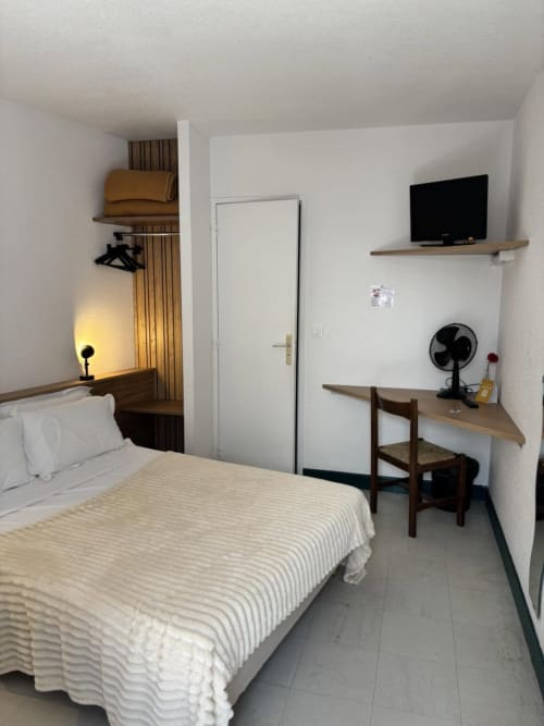 Chambre d'hôtel compacte à l'Hôtel Du Rocher avec lit simple, bureau, TV, ventilateur et équipements modernes à Le Caylar