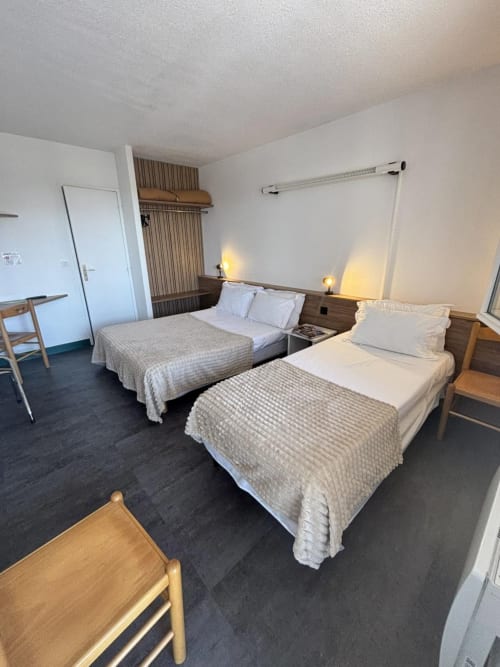 Chambre Triple Confort à l'Hôtel Du Rocher au Caylar avec deux lits, mobilier en bois et vue sur la ville