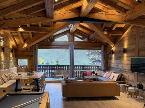 Intérieur luxueux d'un chalet en bois à La Plagne avec vue montagne, canapé cuir et poutres apparentes