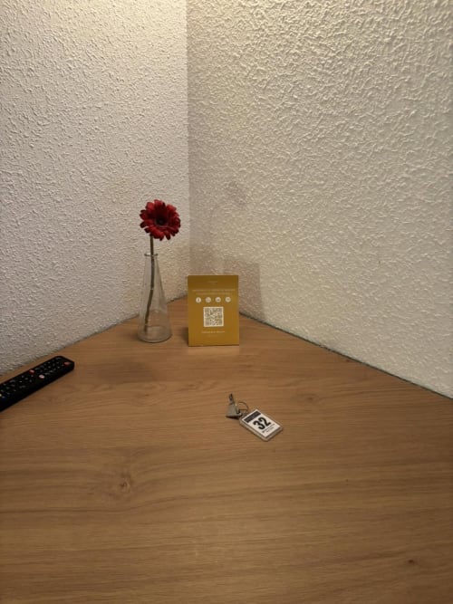 Coin minimaliste d'une chambre d'hôtel à l'Hôtel Du Rocher avec gerbera rouge, boîte dorée, télécommande et porte-clés sur un bureau en bois