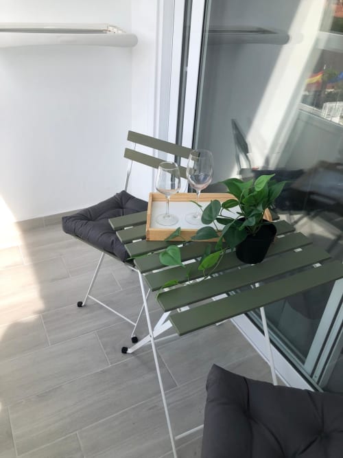 Zona de estar moderna en balcón de Apartamentos Aloe con sillas verdes, copas de vino y plantas decorativas con vistas a la piscina