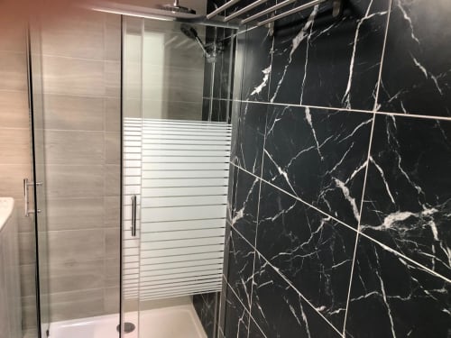 Baño moderno en Apartamentos Aloe con azulejos de mármol negro, cabina de ducha de cristal y puertas de panel esmerilado