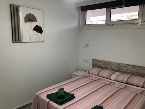 Moderno dormitorio en Apartamentos Aloe de Playa del Inglés con ropa de cama a rayas rosa, cabecero de madera y arte floral en la pared