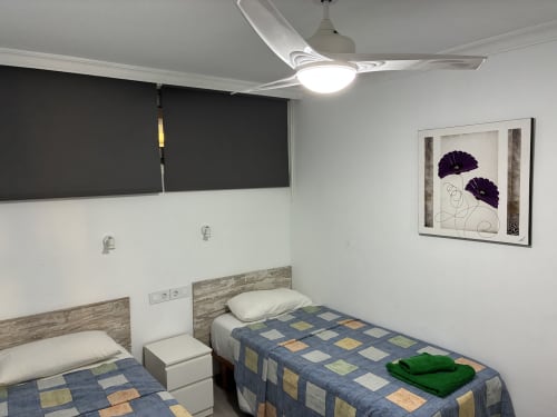 Dormitorio doble en el apartamento Aloe Suite de Playa del Inglés con ventilador moderno, cuadros decorativos en la pared y colchas azules patchwork