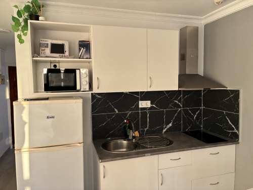 Moderna cocina en suite Aloe con muebles color crema, backsplash de mármol negro, lavabo y refrigerador blanco