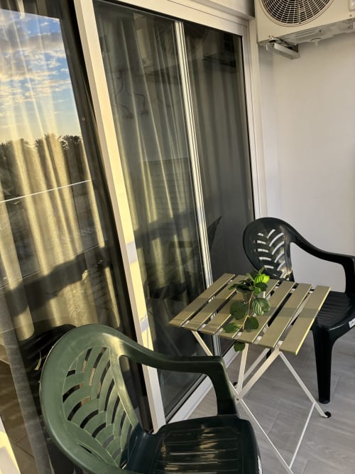 Soleado balcón de Apartamentos Aloe con silla verde, mesita y planta en maceta con vista a palmeras